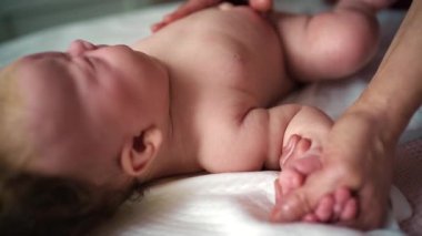 Bebek sırt üstü yatarken bir yetişkin onlara masaj yapar ve bebeğin elini nazikçe tutar.