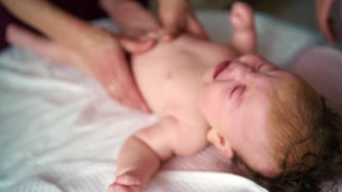 Bebek sırt üstü yatarken bir yetişkin onlara masaj yapıyor ve anne nazikçe bebeğin elini tutuyor.