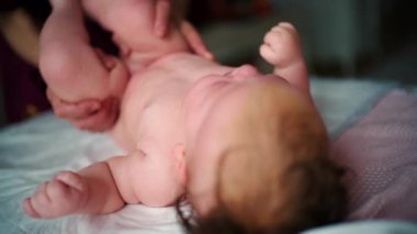 Bebek sırt üstü yatarken bir yetişkin onlara masaj yapar ve bebeğin elini nazikçe tutar.