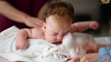 Yumuşak bir oyuncakla masaj yaparken ağlayan bir bebeğin dikkatini dağıtmaya çalışan bir kadın.