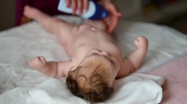 Bebek bakıcısı şişeden bebek yağı sürerken ve bebeğe masaj yaparken yumuşak bir yatakta uzanan bir bebek.