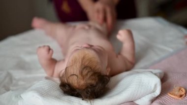 Bebek bakıcısı bebeğe masaj yaparken yumuşak bir yatakta uzanan bir bebek.