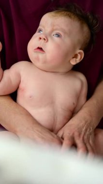 Bebek dik otururken, bir bakıcı tarafından destekleniyor. Dikey