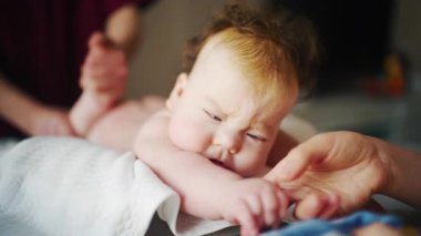 Close up of a baby while an adult gently supports them during a home care routine