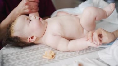 Bebek yatakta rahatça yatar, yukarıya bakar. Bakıcı ve anne ise yakınlarda hareket egzersizleri yapar.
