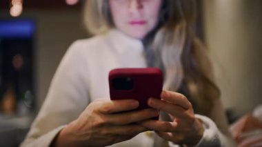 Kapalı bir yerde, akşam ışığında akıllı telefon kullanan bir kadına yaklaş.