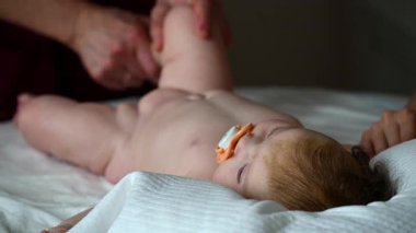 Bebek yatakta rahatça yatar, yukarıya bakar. Bakıcı ve anne ise yakınlarda hareket egzersizleri yapar.