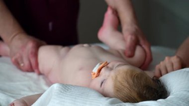 Bebek yatakta rahatça yatar, yukarıya bakar. Bakıcı masaj yapar ve hareketlilik egzersizleri yapar.