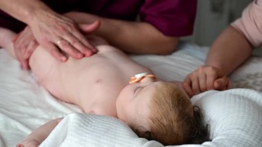 Bebek sırt üstü yatarken bir yetişkin onlara masaj yapıyor ve anne nazikçe bebeğin elini tutuyor.