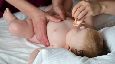 Bebek sırt üstü yatarken bir yetişkin onlara masaj yapıyor ve anne nazikçe bebeğin elini tutuyor.