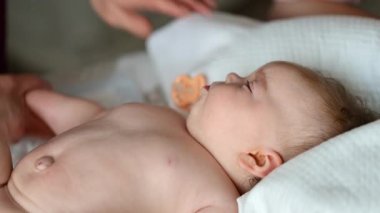 Bebek sırt üstü yatarken bir yetişkin onlara masaj yapıyor ve anne nazikçe bebeğin elini tutuyor.