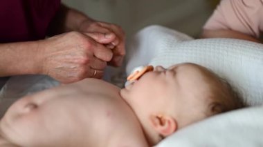 Bebek sırt üstü yatarken bir yetişkin onlara masaj yapıyor ve anne nazikçe bebeğin elini tutuyor.