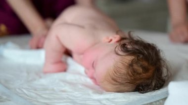 Bebek karnının üstünde yatarken bir yetişkin onlara masaj yapıyor ve hareket egzersizleri yapıyor.
