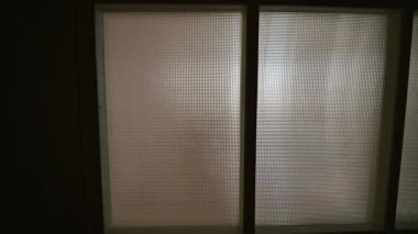 Yumuşak ışığa doğru hareket eden kamera, karanlık bir iç koridordaki buzlu cam kapıdan içeri doğru parlıyordu.