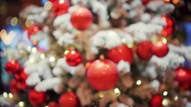 Süslü Noel ağacı, kırmızı süsler, karla kaplı dallar ve arka planda parlak ışıklar.