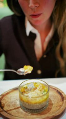 Bir kaşık kullanarak cam bardakta chia pudingi yiyen bir kadın. Dikey