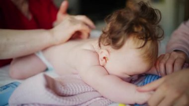 Bebek karnının üstünde yatarken bir yetişkin onlara masaj yapıyor ve hareket egzersizleri yapıyor.