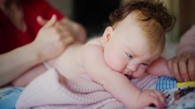 Bebek karnının üstünde yatarken bir yetişkin onlara masaj yapıyor ve hareket egzersizleri yapıyor.