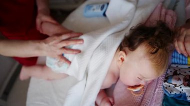 Bebek karnının üstünde yatarken bir yetişkin onlara masaj yapıyor ve hareket egzersizleri yapıyor.