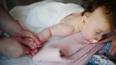 Bebek sırt üstü yatarken bir yetişkin onlara masaj yapıyor ve anne de emziği bebeğin ağzında tutuyor.