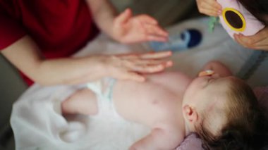 Bir yetişkin bebeğin vücuduna losyon ya da yağ sürerken bebek sırt üstü uzanıyor.