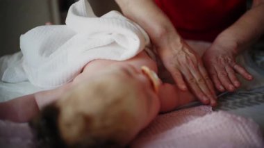 Bebek sırt üstü yatarken bir yetişkin onlara masaj yapıyor ve anne de emziği bebeğin ağzında tutuyor.