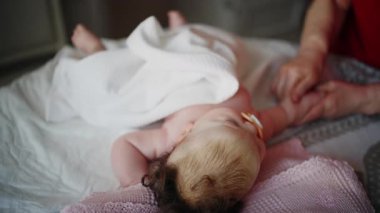 Bebek sırt üstü yatarken bir yetişkin onlara masaj yapıyor ve anne de emziği bebeğin ağzında tutuyor.