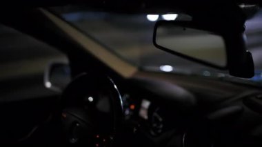 Gece çekilen iç araba dışarıda bulanık şehir ışıkları olan gösterge paneli ve dikiz aynasını gösteriyor.
