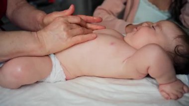 Bebek sırtüstü yatarken bir bakıcı bebeğin üst vücuduna nazikçe masaj yapar.