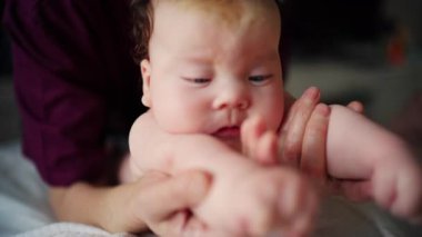 Caregiver gently stretching a baby's arms while the infant lies on a padded surface