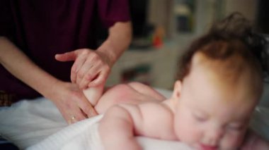 Bebek karnının üstünde yatarken bir yetişkin onlara masaj yapıyor ve hareket egzersizleri yapıyor.