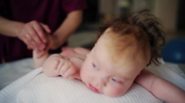 Bebek karnının üstünde yatarken bir yetişkin onlara masaj yapıyor ve hareket egzersizleri yapıyor.