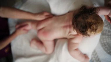 Bebek karnının üstünde yatarken bir yetişkin onlara masaj yapıyor ve hareket egzersizleri yapıyor.