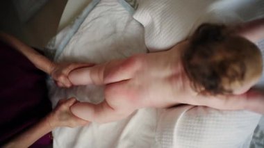 Bebek karnının üstünde yatarken bir yetişkin onlara masaj yapıyor ve hareket egzersizleri yapıyor.