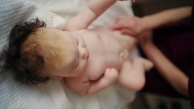 Bebek sırt üstü yatarken bir yetişkin onlara masaj yapıyor ve hareket egzersizleri yapıyor.