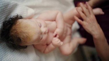 Bebek sırt üstü yatarken bir yetişkin onlara masaj yapıyor ve hareket egzersizleri yapıyor.