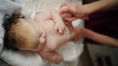 Bebek sırt üstü yatarken bir yetişkin onlara masaj yapıyor ve hareket egzersizleri yapıyor.