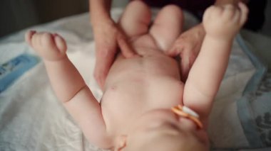 Bebek sırt üstü yatarken bir yetişkin onlara masaj yapıyor ve hareket egzersizleri yapıyor.