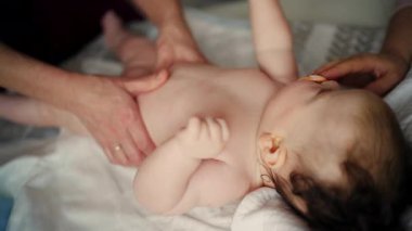Bebek sırt üstü yatarken bir yetişkin onlara masaj yapıyor ve anne de emziği bebeğin ağzında tutuyor.