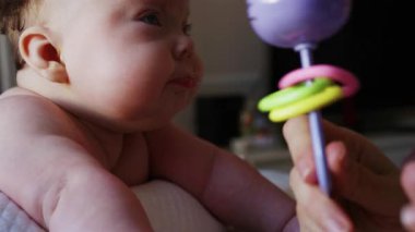 Masaj sırasında oyuncak ile battaniyeye uzanmış ağlayan bir bebeğin dikkatini dağıtmaya çalışan bir kadın.