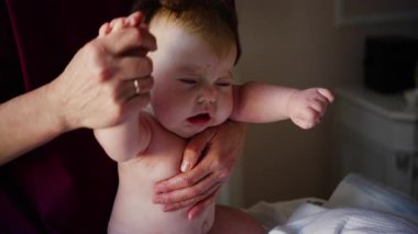 Caregiver supporting a baby upright while holding their hands. Early development and physical support during infancy