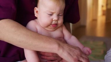 Bebek bakıcısı gelişim egzersizi sırasında bebeği dik tutarken bir diğer yetişkin de yakınlarda bir oyuncakla meşgul oluyor.