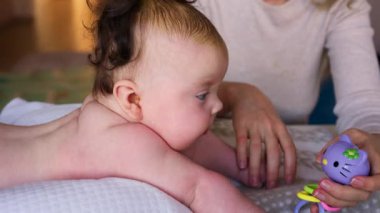 Bebek yumuşak bir yastıkta yatarken anne renkli bir çıngırak kullanarak bebekle oynuyor.