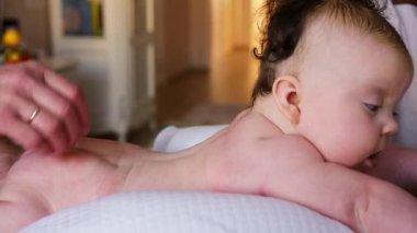 Bebek karnının üstünde yatarken bir yetişkin onlara masaj yapıyor ve hareket egzersizleri yapıyor.