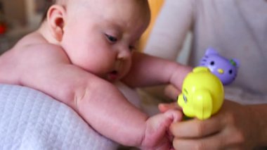 Masaj sırasında oyuncak ile battaniyeye uzanmış ağlayan bir bebeğin dikkatini dağıtmaya çalışan bir kadın.