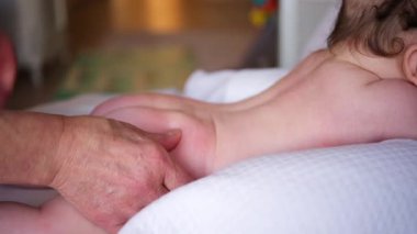 Bebek karnının üstünde yatarken bir yetişkin onlara masaj yapıyor ve hareket egzersizleri yapıyor.