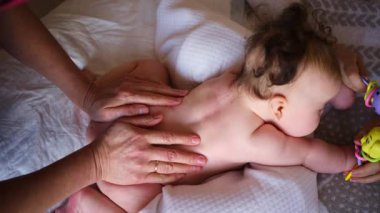 Bebek karnının üstünde yatarken bir yetişkin onlara masaj yapıyor ve hareket egzersizleri yapıyor.