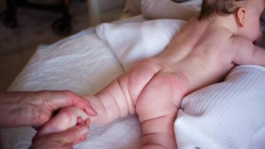 Bebek karnının üstünde yatarken bir yetişkin onlara masaj yapıyor ve hareket egzersizleri yapıyor.