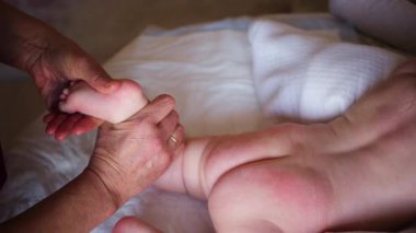 Bebek karnının üstünde yatarken bir yetişkin onlara masaj yapıyor ve hareket egzersizleri yapıyor.