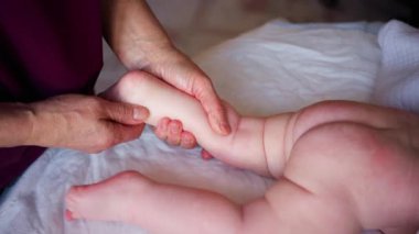 Bebek karnının üstünde yatarken bir yetişkin onlara masaj yapıyor ve hareket egzersizleri yapıyor.